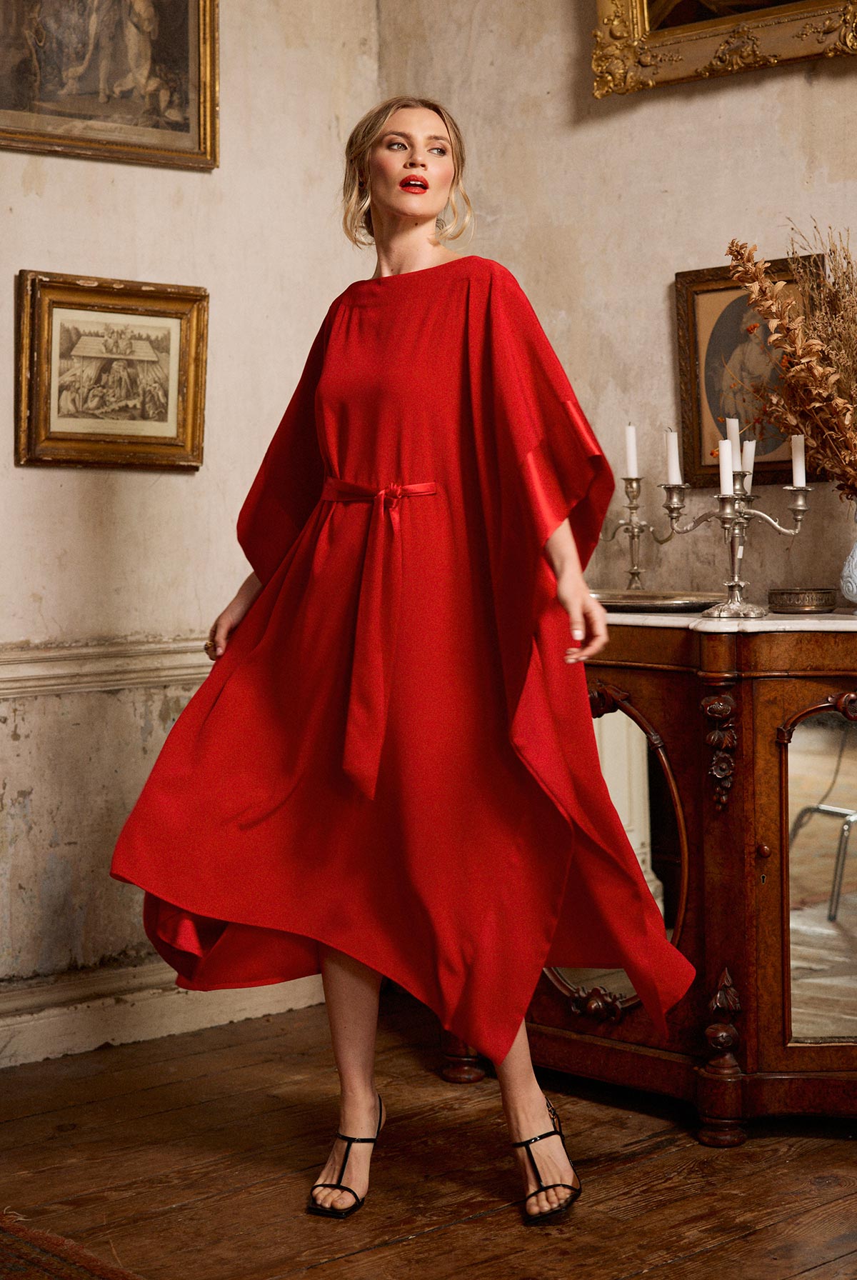 Woman in a red dress standing in an elegant room with classical decor.