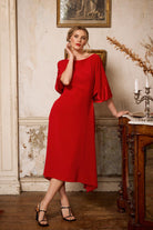 Woman in a red dress standing in an elegant room with a candle and decorative elements.