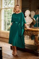 Woman in a green dress standing in an elegant room with classical decor.