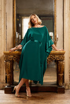 Woman in a teal dress standing in front of a large mirror in an elegant room.