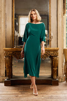 Woman in a green dress standing in front of a large mirror in an elegant room.