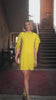 Video of a woman in a yellow dress standing in an indoor setting 
