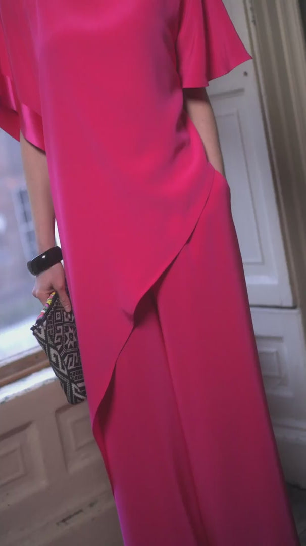 Woman in a bright pink dress holding a colorful handbag indoors.