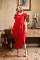Woman in a red dress standing in an elegant room with a piano and framed picture.
