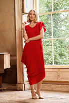 Woman in a red dress standing in a room with large windows.
