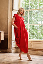Woman in a red dress standing in a room with large windows and wooden floor.