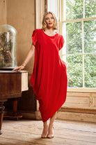 Woman in a red dress standing in a room with wooden floor and large window