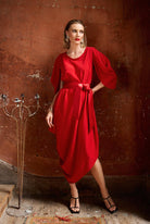 Woman in a red dress standing against a textured brown wall.