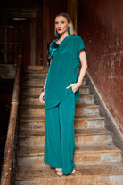Woman in a teal outfit standing on a staircase with a rustic wall background
