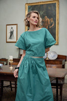 Woman wearing a teal outfit in an elegant room with paintings on the wall.