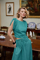 Woman in a teal dress standing in an elegant room with paintings on the wall.