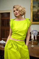 Woman wearing a bright lime yellow outfit in an indoor setting with a painting in the background