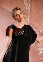 Woman wearing a black dress with colorful embellishments against a textured pink wall.