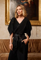 Woman in a black outfit standing in a room with a painting in the background