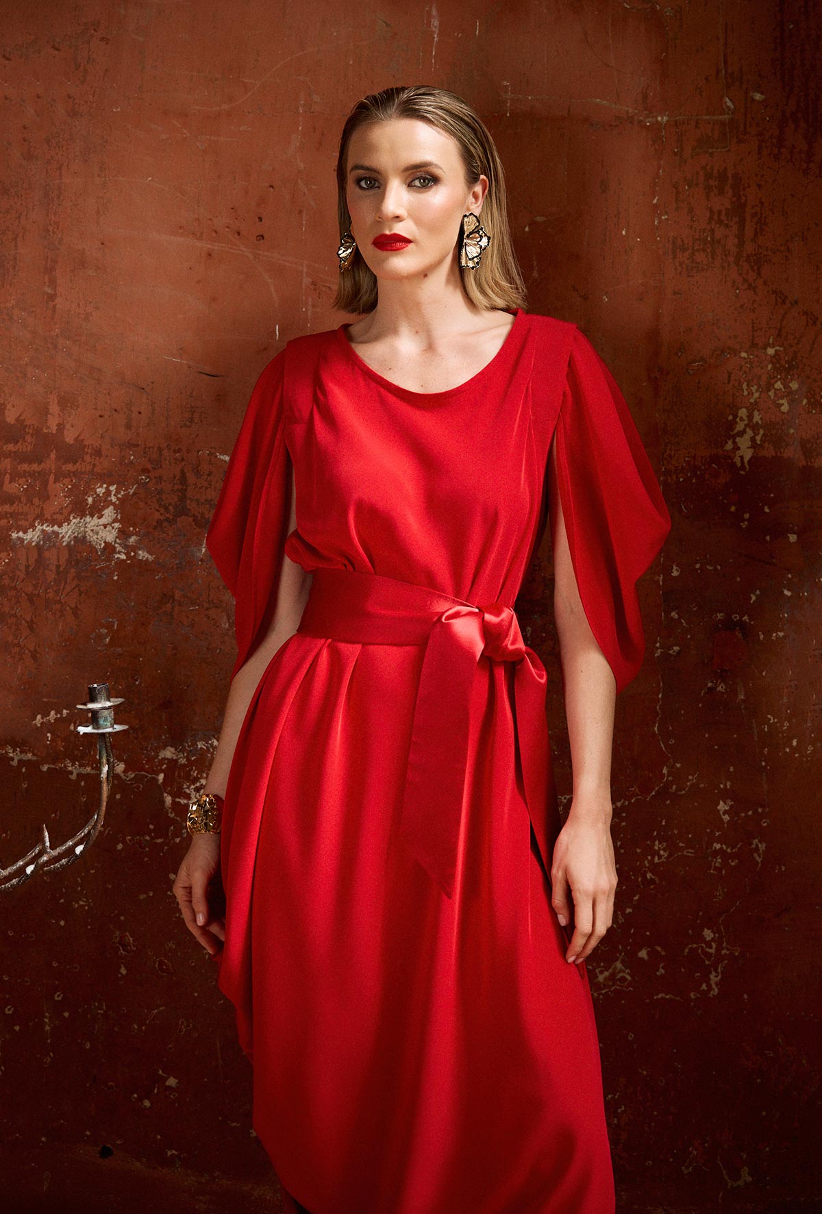 Woman wearing a red dress with a belt against a textured brown wall